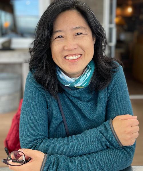 Asian woman in turquoise sweater smiling with arms crossed