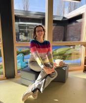 Image of woman with red glasses, brown hair, and striped sweater seated in a preschool classroom