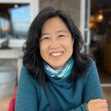 Asian woman in turquoise sweater smiling with arms crossed